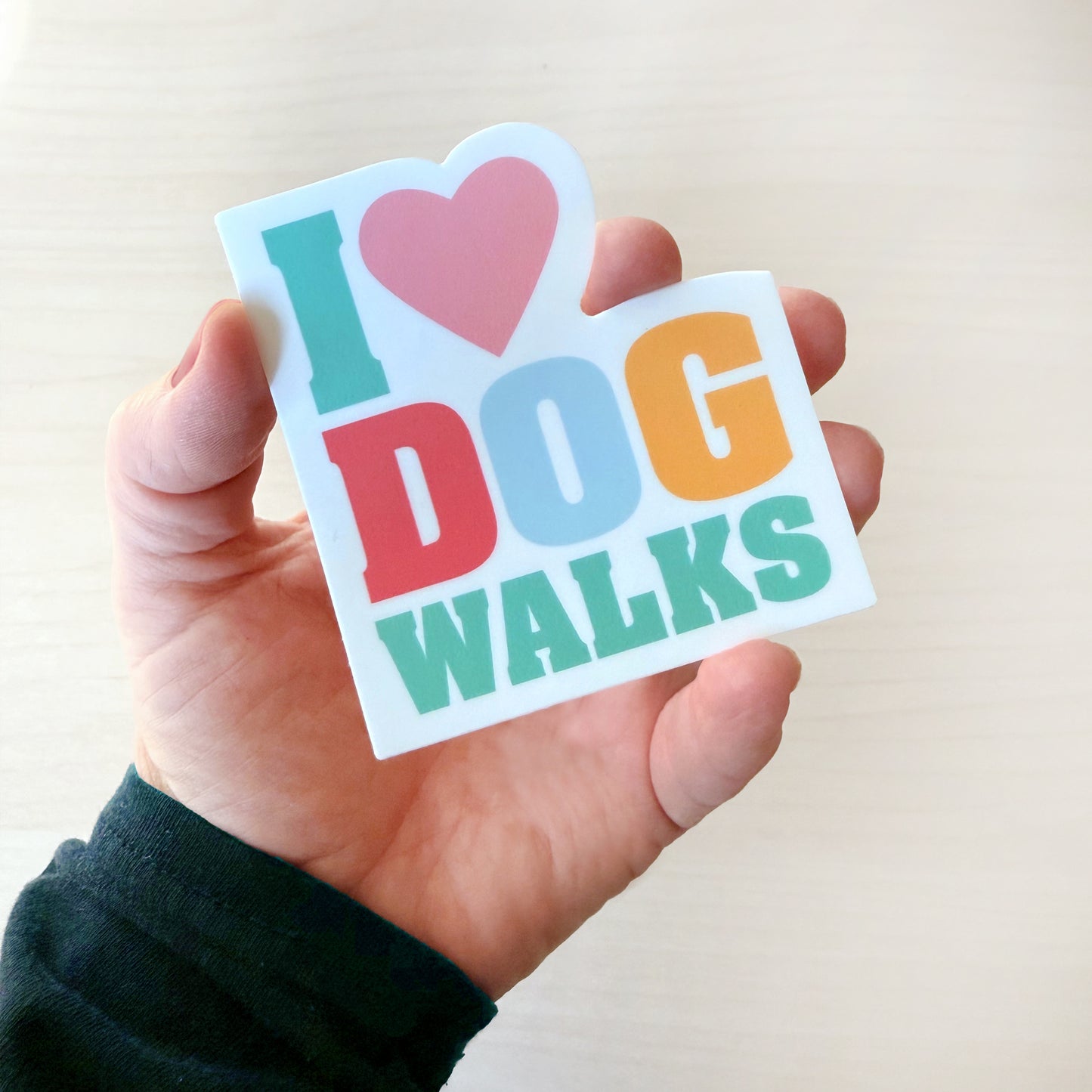 Hand holding a colorful sticker with 'I ❤️ DOG WALKS' text against a light background