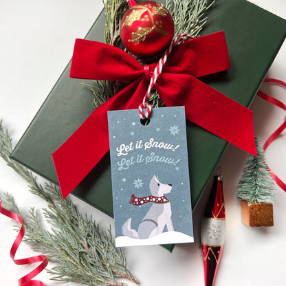 Decorative gift box with a red ribbon, Christmas tree branch, and 'Let it Snow' tag.