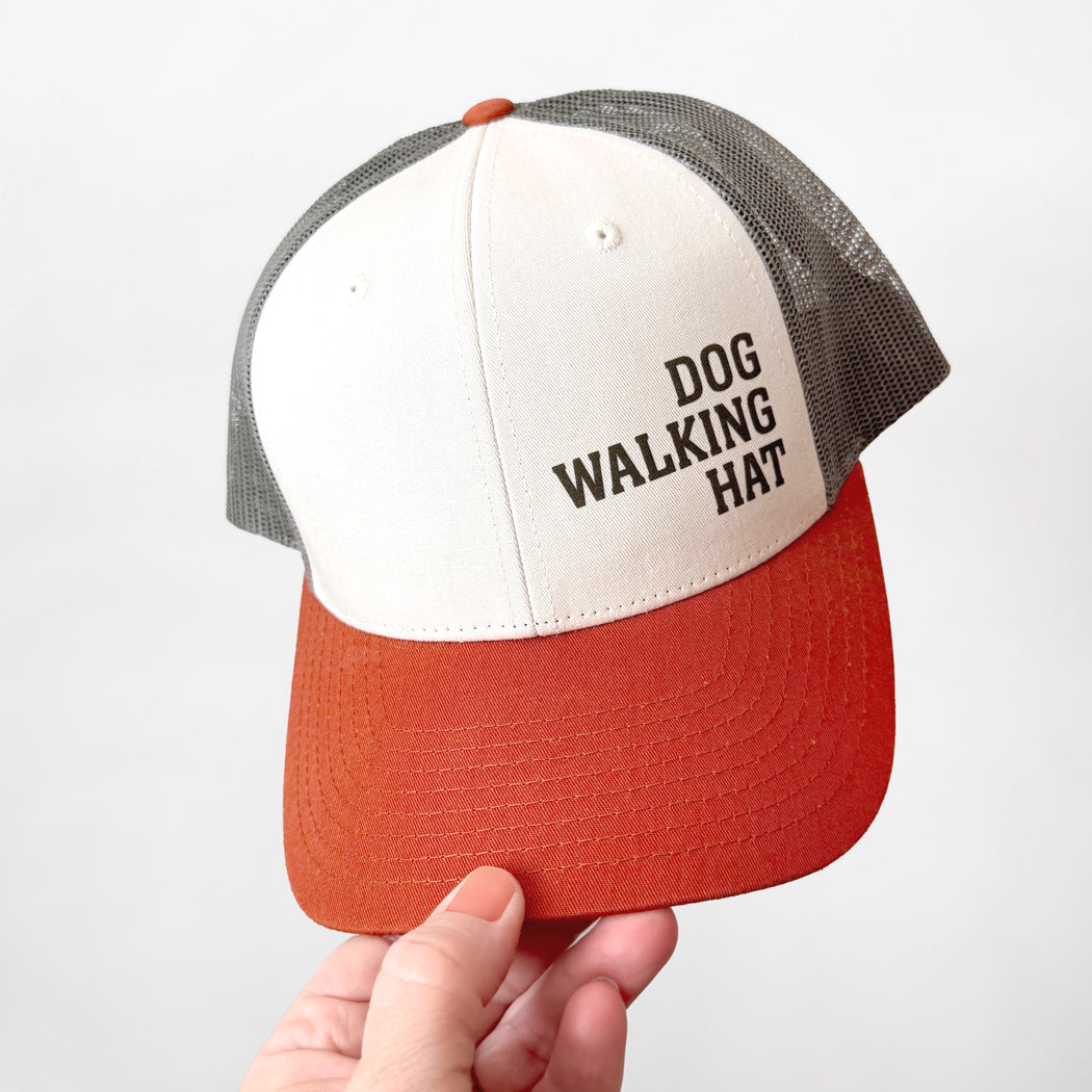Cap with 'DOG WALKING HAT' text held by a hand against a white background