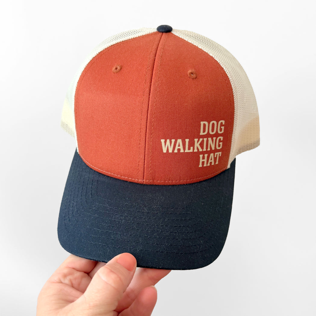 Cap with 'Dog Walking Hat' text held by a hand on a white background