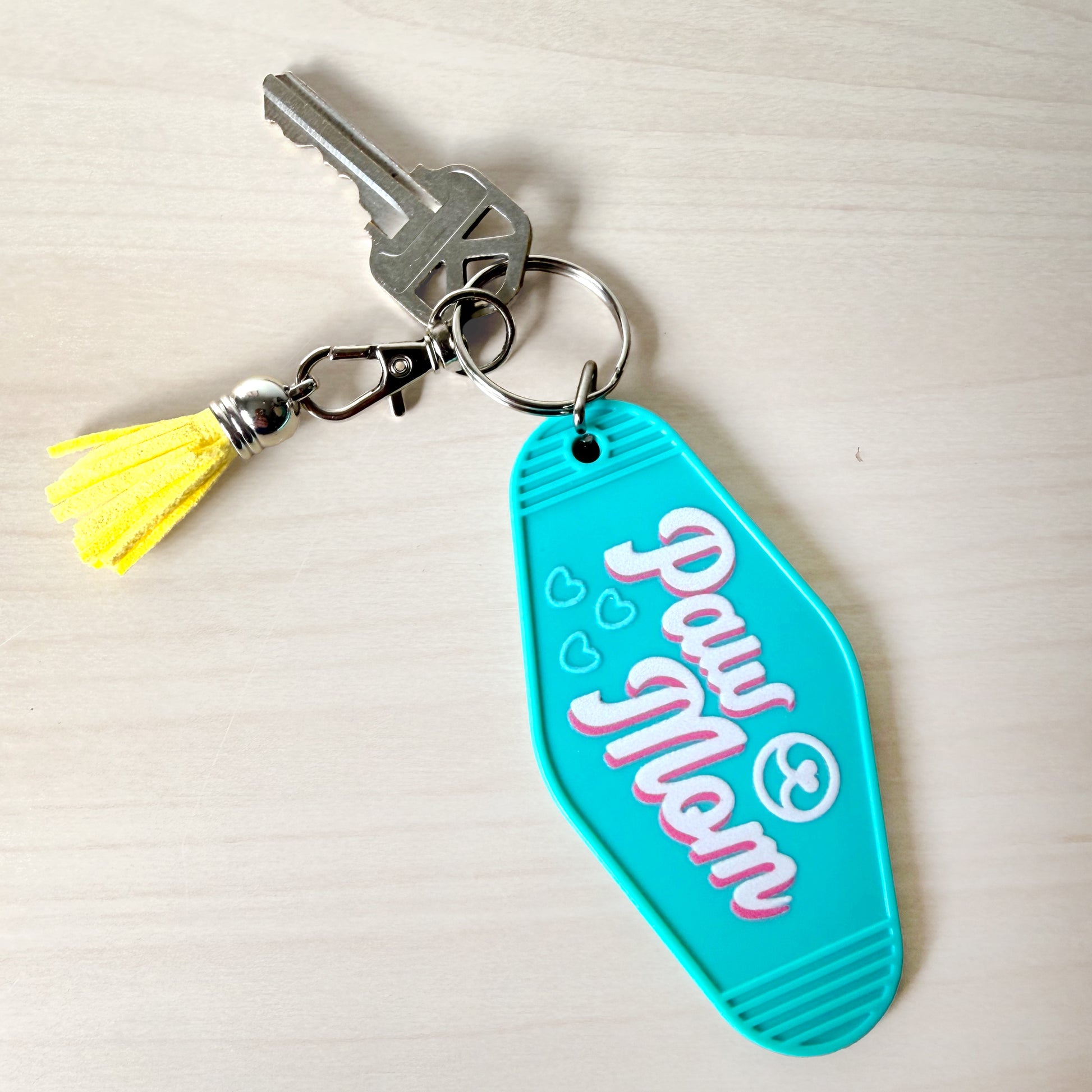 Turquoise keychain with 'Paw Mom' text and yellow tassel on a light background