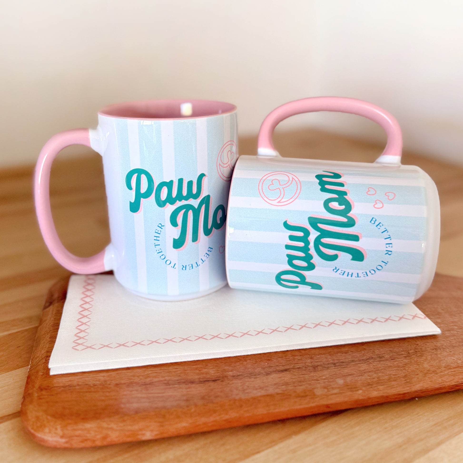 Two mugs with 'Paw Mom' text on a wooden surface