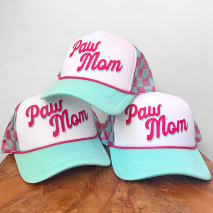 Three 'Paw Mom' hats with plaid brims on a wooden surface.