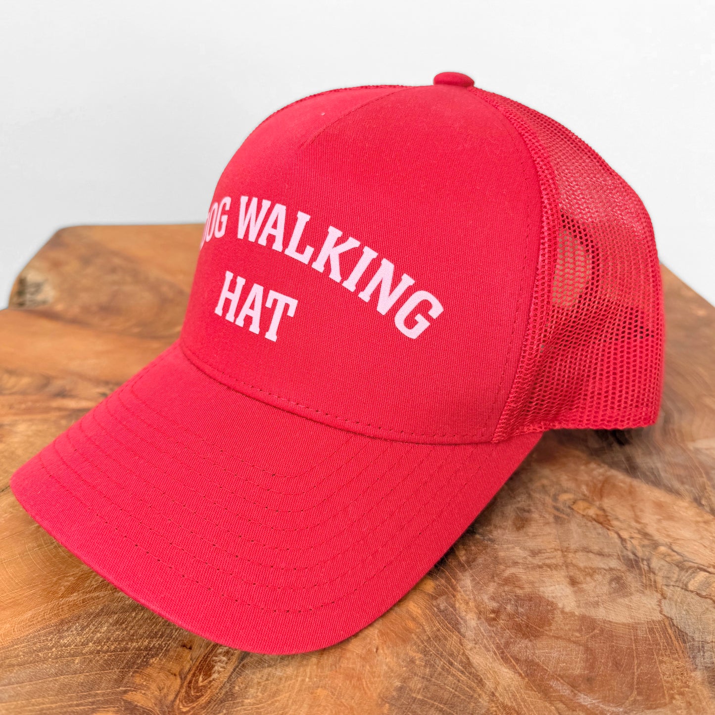 Red cap with 'DOG WALKING HAT' text on a wooden surface