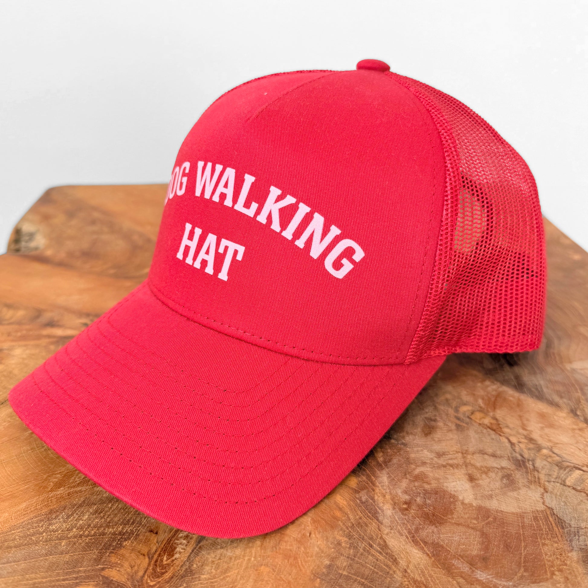 Red cap with 'DOG WALKING HAT' text on a wooden surface