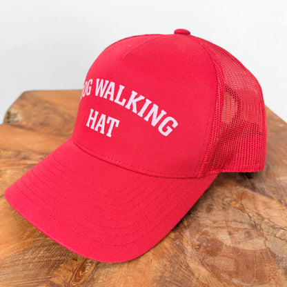 Red cap with 'DOG WALKING HAT' text on a wooden surface
