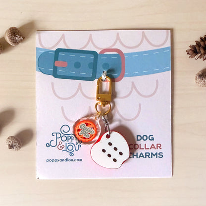 A dog collar charm set displayed on its branded backing card. The set includes a gold lobster clasp, a round orange and white patterned charm, and a white die-cut charm shaped like a six-sided die with black dots.