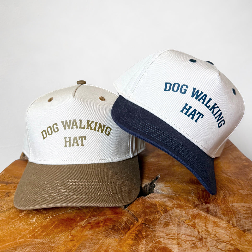 Two hats with 'DOG WALKING HAT' text on a wooden surface.