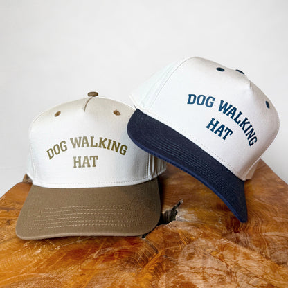Two hats with 'DOG WALKING HAT' text on a wooden surface.