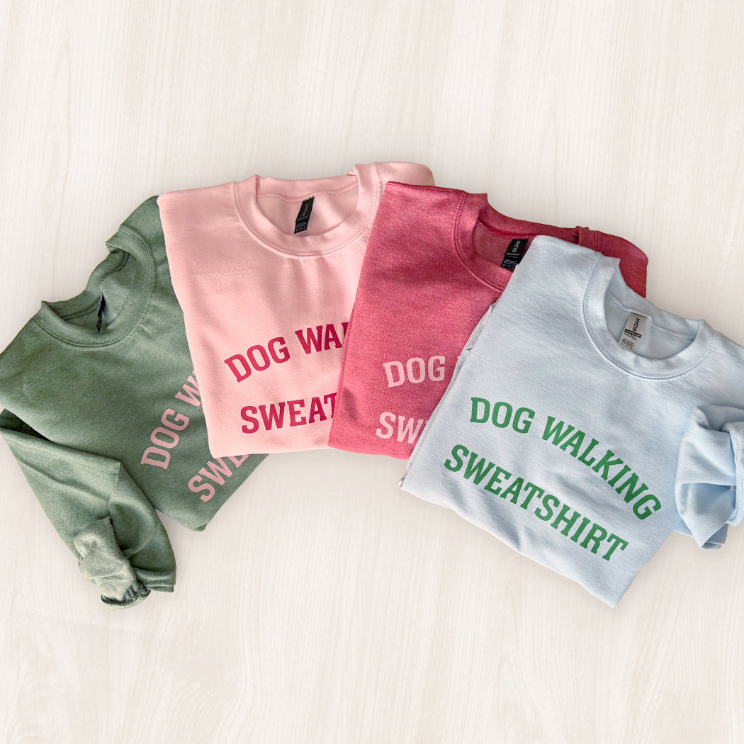 Four folded sweatshirts in green, pink, red, and blue with 'DOG WALKING SWEATSHIRT' text on a light background.
