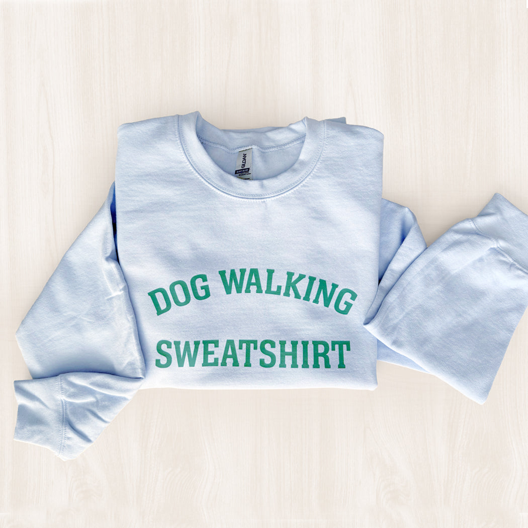 Light blue sweatshirt with 'DOG WALKING SWEATSHIRT' text on a light wooden surface