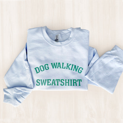 Light blue sweatshirt with 'DOG WALKING SWEATSHIRT' text on a light wooden surface