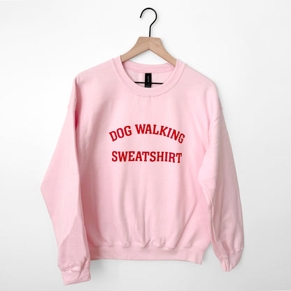 Pink sweatshirt with 'DOG WALKING SWEATSHIRT' text on a hanger against a white background