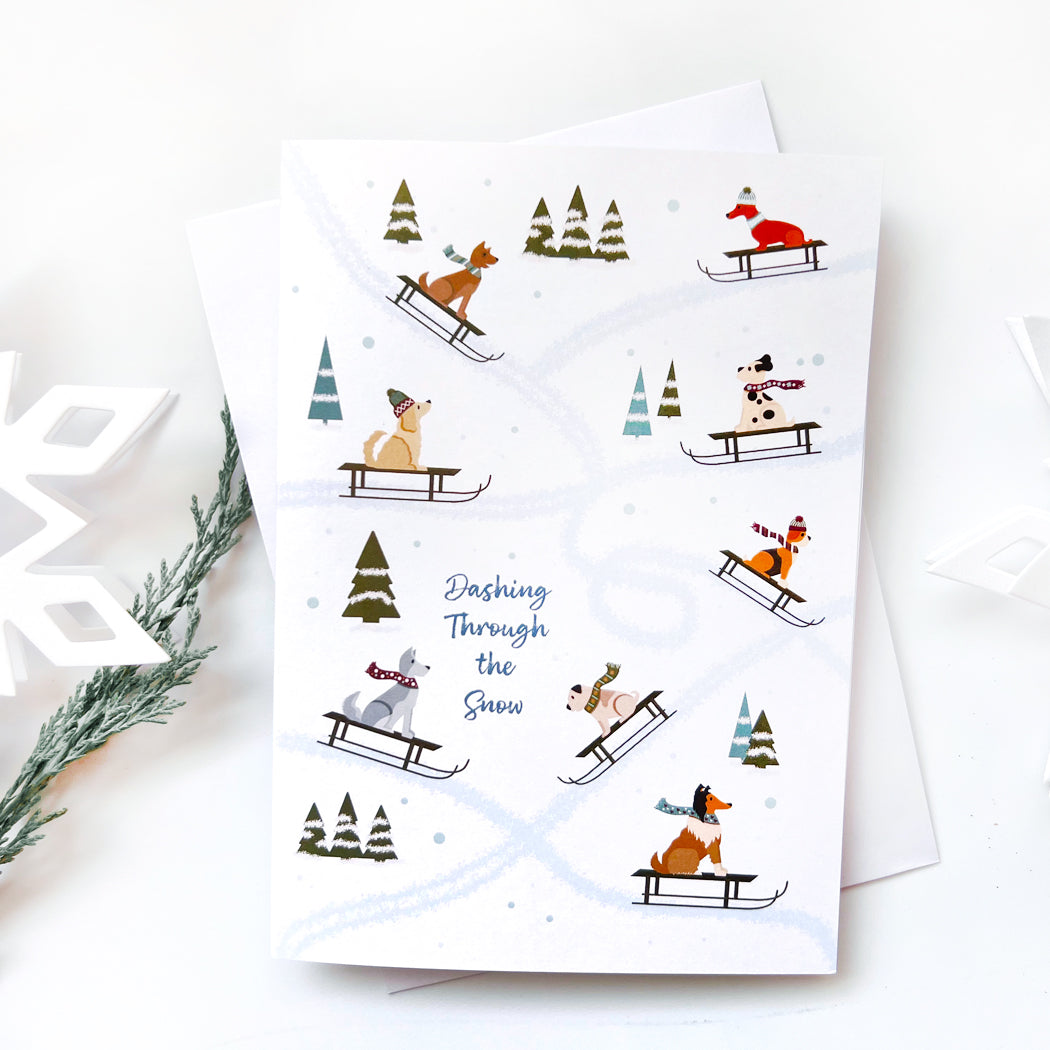 Front view of Dog Sledding Winter Card featuring illustrated dogs sledding through a snowy landscape.