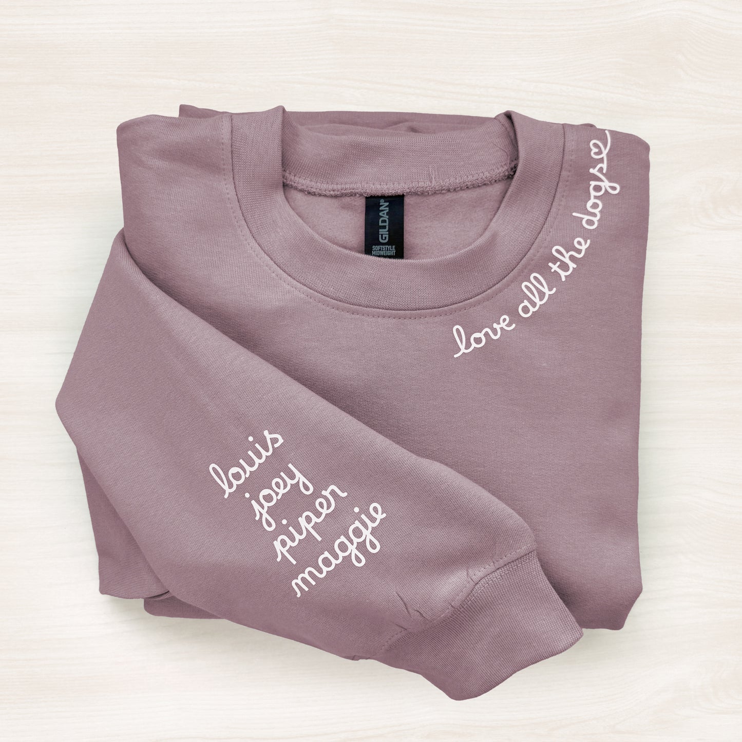 Folded mauve sweatshirt with names printed on a white background