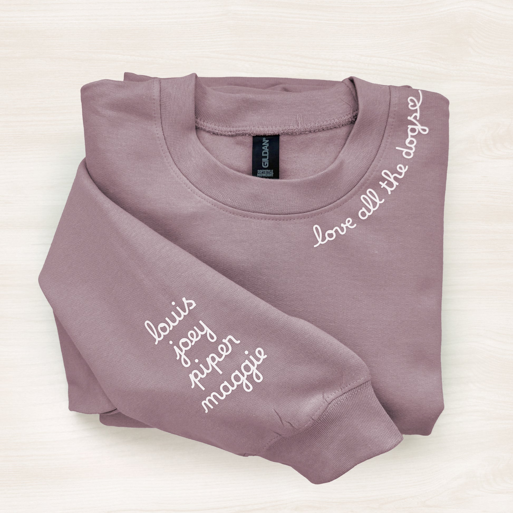 Folded mauve sweatshirt with names printed on a white background