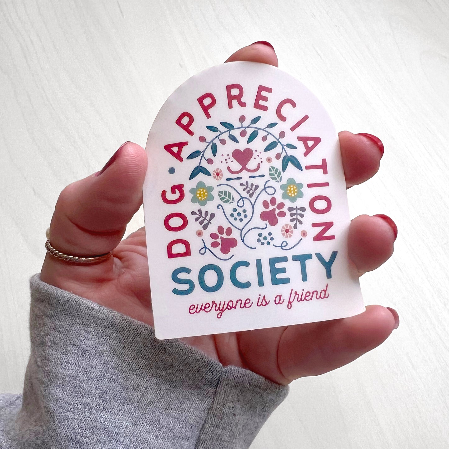 Front view of Dog Appreciation Society Sticker with dog nose, paws, flower, leaves, and hearts design.