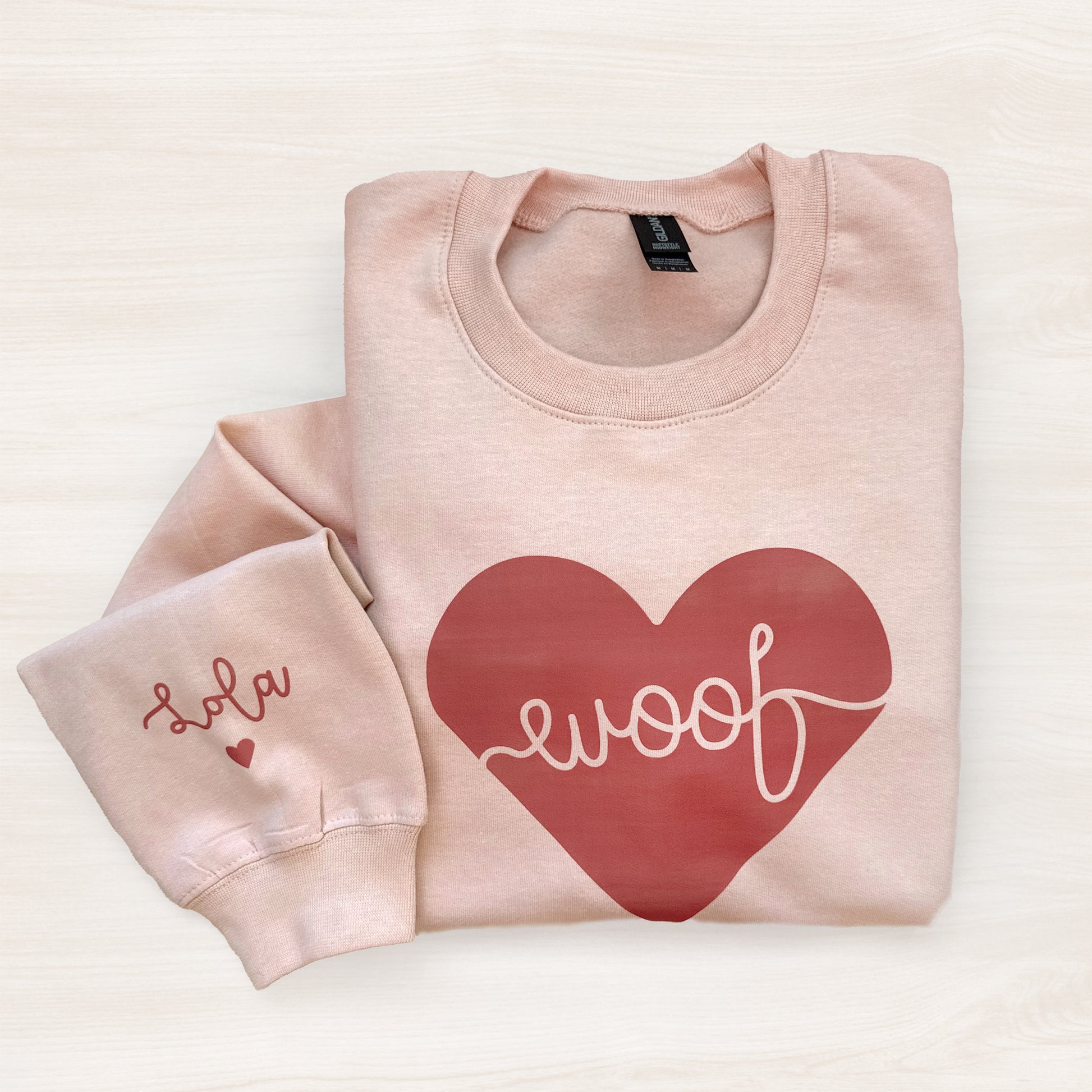 Folded pink sweatshirt with a red heart and 'woof' text on a light background
